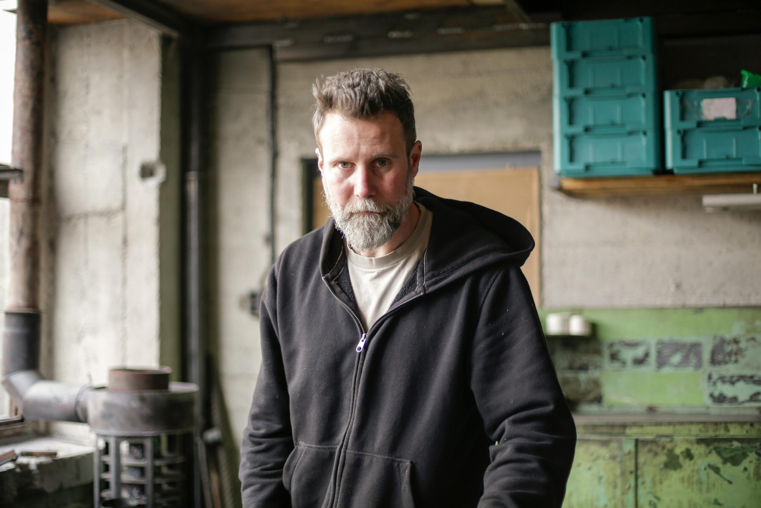 Sleep 001 Serious adult bearded mechanic in black workwear standing in spacious workshop and looking at camera
